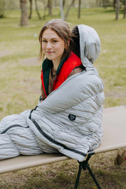 Grey goose down sleeping bag with person sitting inside, showcasing warmth and comfort for outdoor use.