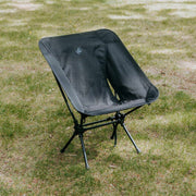 Low back ultralight black folding camping chair with storage pouch on grass.